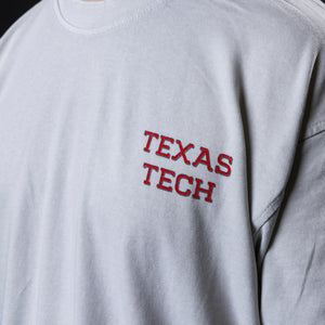 Close-up of a light gray t-shirt featuring 'TEXAS TECH wordmark screen-printed on the left chest