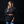 A woman modeling a black crewneck sweatshirt with a red 'TECH'  pennant logo on the chest, paired with blue jeans, set against a solid black studio background.