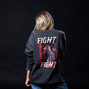 A woman viewed from behind wearing a dark charcoal gray sweatshirt with a large graphic print on the back. The graphic features the words 'FIGHT RAIDERS FIGHT' and an archival image of the Masked Rider